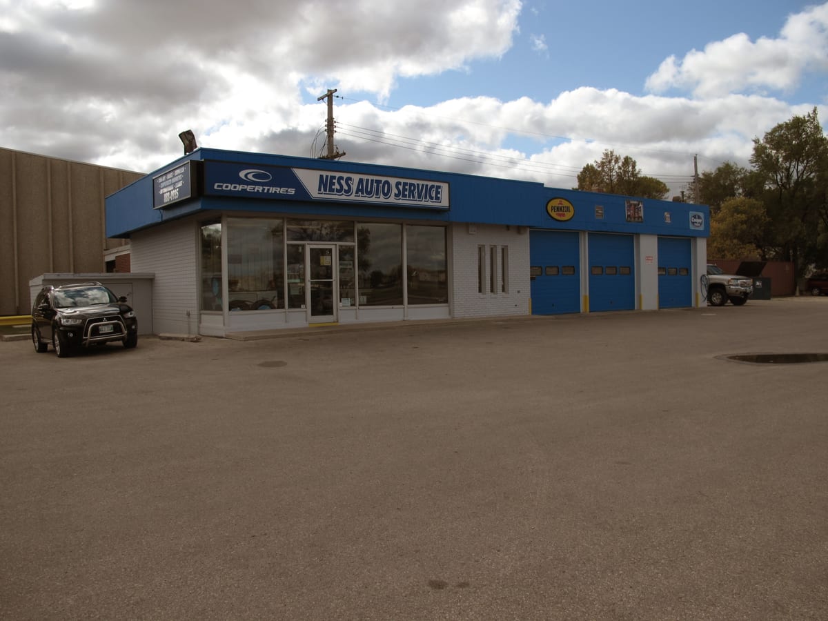 The Ness Auto Service building from the parking lot: a blue fascia with the name, the office windows and three blue bay doors