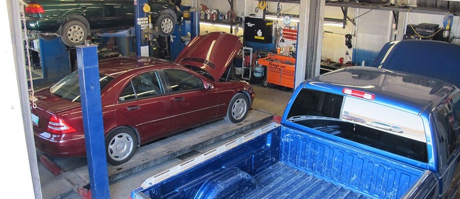 Inside the shop: a car on one lift and a blue pickup in the next bay, tool chests along the wall